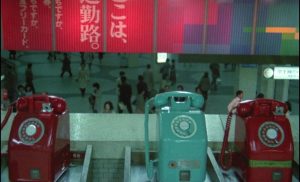 Trois vieux téléphones, deux rouges et un bleu turquoise, dans une gare du Japon, scène du film Sans soleil.