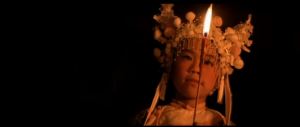 Un enfant avec le couvre-chef traditionnel chinois tout blanc, s'éclaire dans la nuit noire avec une petite flamme au bout d'un encens, scène du film Il était une fois en Chine.