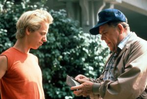 Un quinquagénaire a casquette bleue sort un billet de son porte-feuille qu'il s'apprête à donner à un jeune blond en marcel rouge face à lui, scène du film Casebusters sur Disney +.