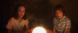 Une boule de lumières fascine les deux enfants protagonistes du film La dernière vie de Simon, assis sur le lit de leur chambre.