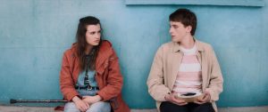 Les personnages Madeleine et Thomas Durant, adolescents, discutent l'air renfrogné, assis sur un banc devant un mur bleu, scène du film La dernière vie de Simon réalisé par Léo Karmann.