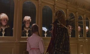Dorothy, vue de dos, est guidée dans une galerie de visages humains vivants posés sur des socles, scène du film Oz un monde merveilleux.