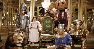 Dorothy, le lion, l'épouvantail, la citrouille et l'homme en fer du Magicien d'Oz tout autour d'un trône dans une salle toute en or, scène du film Oz un monde extraordinaire. 