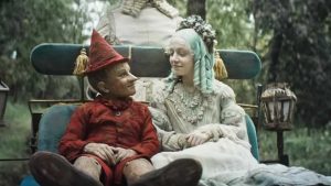 Pinocchio et la Fée Bleue se sourient, assis sur un petit banc dans un parc, scène du film Pinocchio de Matteo Garrone pour notre critique.