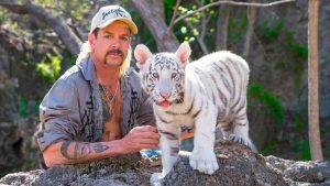 Joe Exotic présente un bébé tigre blanc, debout sur un rocher, scène de la série documentaire Netflix Au royaume des fauves.