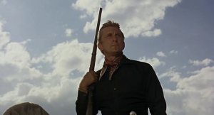 En contre-plongée, Kirk Dougas regarde l'horizon, sous le ciel du Mexique, son fusil contre son épaule, scène du film El Perdido.