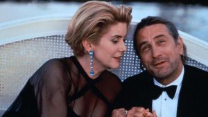 Catherine Deneuve et Robert de Niro en tenuede soirée, assis sur un banc blanc au plein air, scène du film Les cent et une nuits de Simon Cinéma.