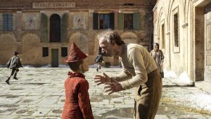 Gepetto (Roberto Benigni) rappelle Pinocchio sur une vieille place ensoleillée, scène du film Pinocchio de Matteo Garrone.