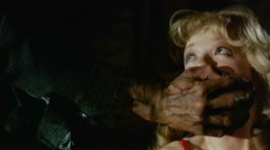 Une patte de monstre sur la bouche d'une jeune femme blonde apeurée, scène du film Hell Night.