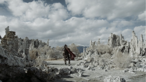 Le guerrier vu de dos traverse une plaine pleine de rochers pointus vers le ciel, scène du film The Head Hunter.