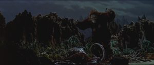 King Kong s'apprête à ramasser des objets perdus sur le sol, de nuit, dans la nature, pour notre histoire de la saga Godzilla.