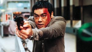 Pao Wai-hung dans une rue de Hong-Kong, le visage ensanglanté, braque son revolver sur quelqu'un hors-champ, scène du film Full Alert.