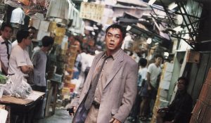 L'acteur Lau Ching-wan bras ballants et yeux écarquillés dans l'étroit marché couvert du film Full Alert pour notre critique.