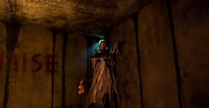 Une silhouette inquiétante au coin d'une salle décrépie, jaune, aux coulées de sang sur les murs, scène du film Mercy Black.
