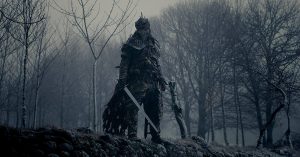Le guerrier à l'armure et masqué du film The Head Hunter pose au milieu d'une forêt grise et brumeuse.