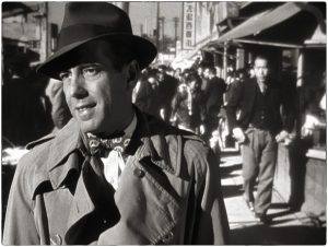 Humphrey Bogart un sourire léger au premier plan, dans les rues de Tokyo en rétroprojection à l'arrière-plan dans le film Tokyo Joe.