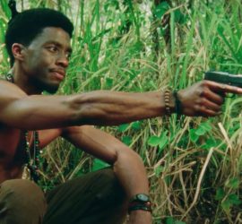 Un jeune soldat américain accroupi, torse nu, dans l'herbe vietnamienne, tient quelqu'un en joue dans le film Da five bloods.