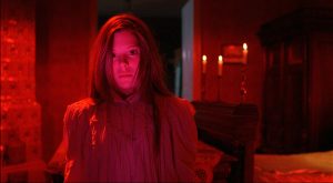 La jeune Dora Szinetar dans une chambre à la lumière rouge, les yeux dans le vide, dans le fond, trois bougies, scène angoissante du film Laurin.
