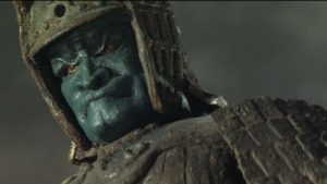 Un géant de pierre vêtu comme un guerrier japonais, au visage renfermé et vert, sous un ciel nuageux, scène de la trilogie Majin.