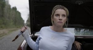 Une femme tient un couteau ensanglanté devant un coffre de voiture ouvert dans lequel on voit un corps allongé, scène du film The Hunt.