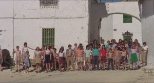 Tous les enfants du village désert du film Les révoltés de l'an 2000 posent debout, les bras le long du corps, devant un bâtiment blanc illuminé par le soleil.