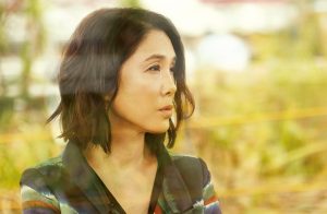 Sur fond d'herbes floues jaunes et vertes, plan rapproché-épaule sur l'actrice Mariko Tsutsui, issu du film L'infirmière.