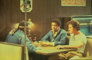 Trois personnages masculins du film Blue Collar dont Harvey Keitel, attablés dans un bar autour d'une bière.