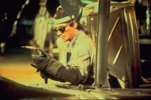 Dans l'usine, un ouvrier-soudeur au travail, avec gants, lunettes de protection et casque.