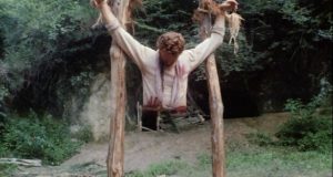 Un homme a les mains liées à deux poteaux de bois, dans la jungle, tout le bas de son corps a été découpé, scène du film Emanuelle et les derniers cannibales.