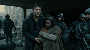 Theo Faron tient dans ses bras la jeune mère Kee, aux côtés de soldats dans les rues en ruines du film Les fils de l'homme.