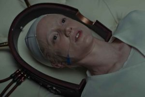 L'actrice Andrea Riseboroug dans une scène du film Possessor où elle est allongée sur une table d'opération, un demi-cercle de cuivre autour de sa tête, prête à prendre possession de l'esprit d'une de ses victimes.