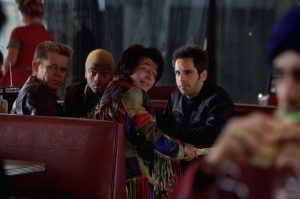 Quatre hommes dont Ben Stiller sont assis dans un dinner, ils se retournent moqueur vers un autre homme assis un peu plus loin qui dévore un burger, scène du film Mystery Men.