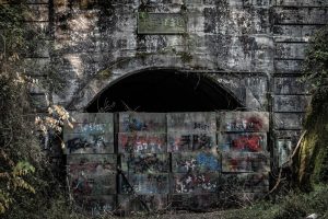 Un vieux tunnel, à moitié obstrué par des pierres anciennes et taggées, plan du film Inunaki.