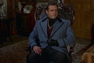 Raymond Burr, l'allure de l'homme riche et cruel, est assis sur le fauteuil de sa chambre, sa main droite est gantée en cuir noir, scène du film L'étreinte du destin.