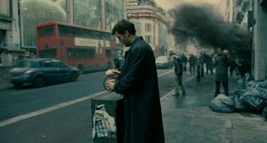 Clive Owen dans les rues grises de Londres, il ne remarque pas la fumée qui s'échappe d'un batiment à sa droite, scène du film Les fils de l'homme.