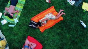 Monica Bellucci bouquine dans un jardin parisien, allongée sur une serviette, autour d'elle d'autres personnes sont allongées comme elle sur une serviette, nous voyons la scène du dessus, plan du film Irréversible inversion intégrale.