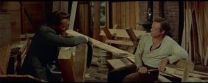 Dans une petite église en cours de construction, deux hommes sont assis face à face, au beau milieu de nombreuses planches de bois, scène du film L'étreinte du destin.
