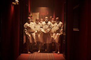 Au bout d'un couloir aux teintes rouges, un groupe d'hommes chauves qui ont l'air d'être des bouchers attendent tout droit, comme prêts à "opérer" scène du film Kadaver.
