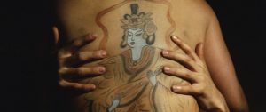 Sur fond noir, deux mains de femmes attrapent les reins d'un dos d'homme sur lequel est tatouée une divinité japonaise, plan d'un film pinku eiga.