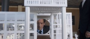 Le visage de Vincent Lindon en costume-cravate vu à travers une maquette architecturale, scène du film Mon cousin réalisé par Jan Kounen.