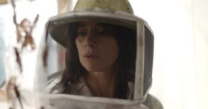 Une femme brune a une mine très inquiète derrière son chapeau d'apicultrice dans le film La nuée.