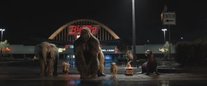 Un éléphant, un gorille, une otarie et trois autres petits animaux à quatre pattes sont sur le parking d'un centre comercial, de nuit, alignés, attendant quelque chose, scène du film Le seul et unique Ivan.