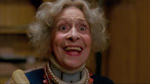Plan rapproché-épaule sur une vieille femme au grand sourire, l'air un peu fou, dans un salon, scène du film Mother's day.