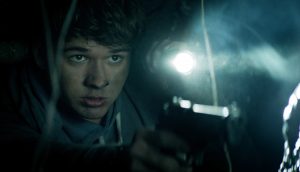L'adolescent Ben, baissé, capuche sur la tête, tend une lampe devant lui, tout au tour de lui la pénombre, scène du film The wretched.