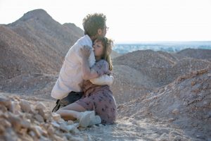 Reda Ketab serre dans ses bras la jeune femme héroïne de la série Possessions, tous deux à terre, usés dans le désert.