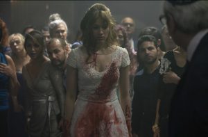 Une jeune femme blonde porte une robe de mariée tâchée de sang, elle a la tête baissée, honteuse, devant les invités, scène de la série Canal + Posessions.