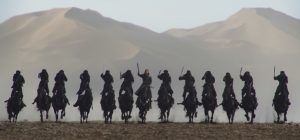 Charge d'un groupe de soldats à cheval, tous alignés, en fond, une grande montagne, scène du film Mulan.