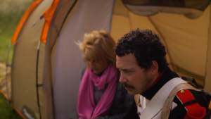 Un homme et une femme, inquiets, sont assis devant une grande tente, scène du film Les héros ne meurent jamais d'Aude Léa Rapin.