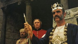 Sean Connery assis sur son trône, avec roi, sceptre, et air sérieux dans le film L'homme qui voulut être roi.
