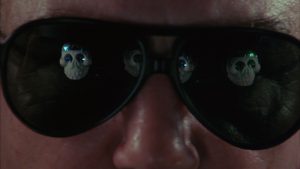 Des crânes squelettiques se reflètent dans des lunettes de soleil aviateur portées par un homme, plan du film Au-dessus du volcan.